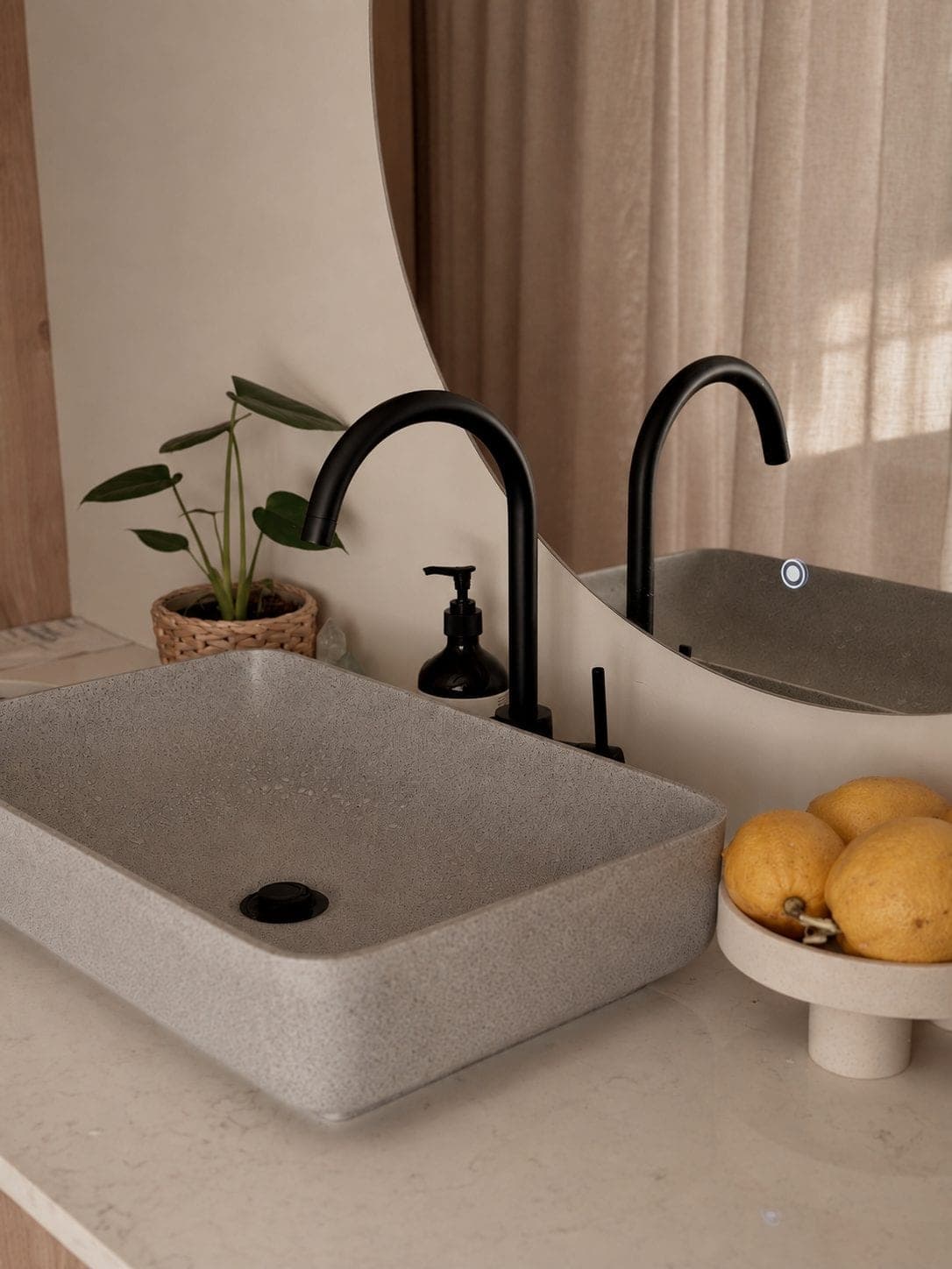 A stone basin with a black tap, a small plant and a bowl of lemons